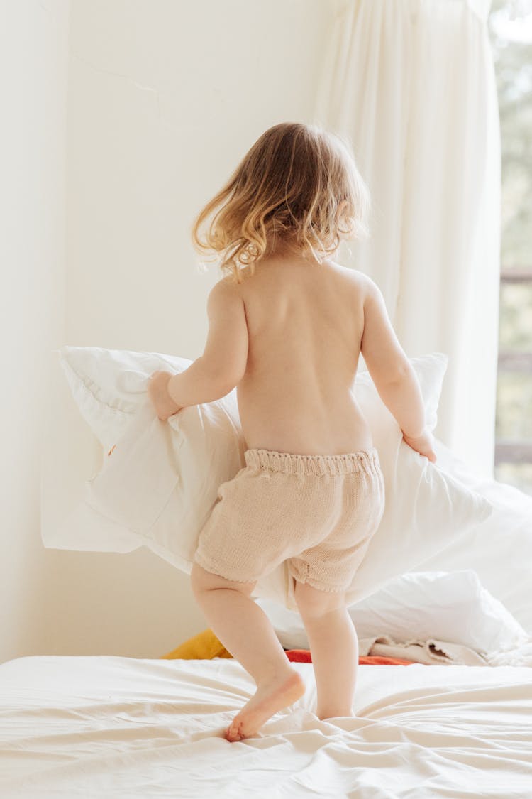 Cute Little Girl Playing With Pillows On Bed At Home