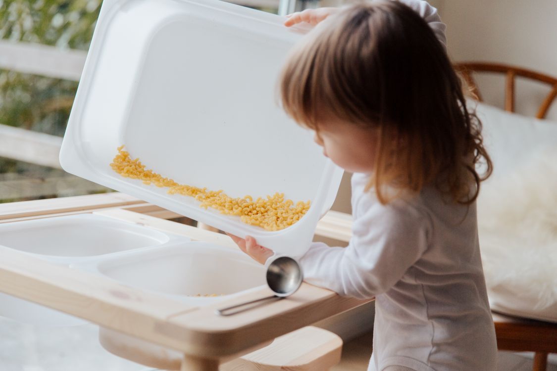 A young child exploring dry pasta in a sensory activity tray