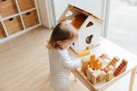Little girl playing with toys at table near window at home