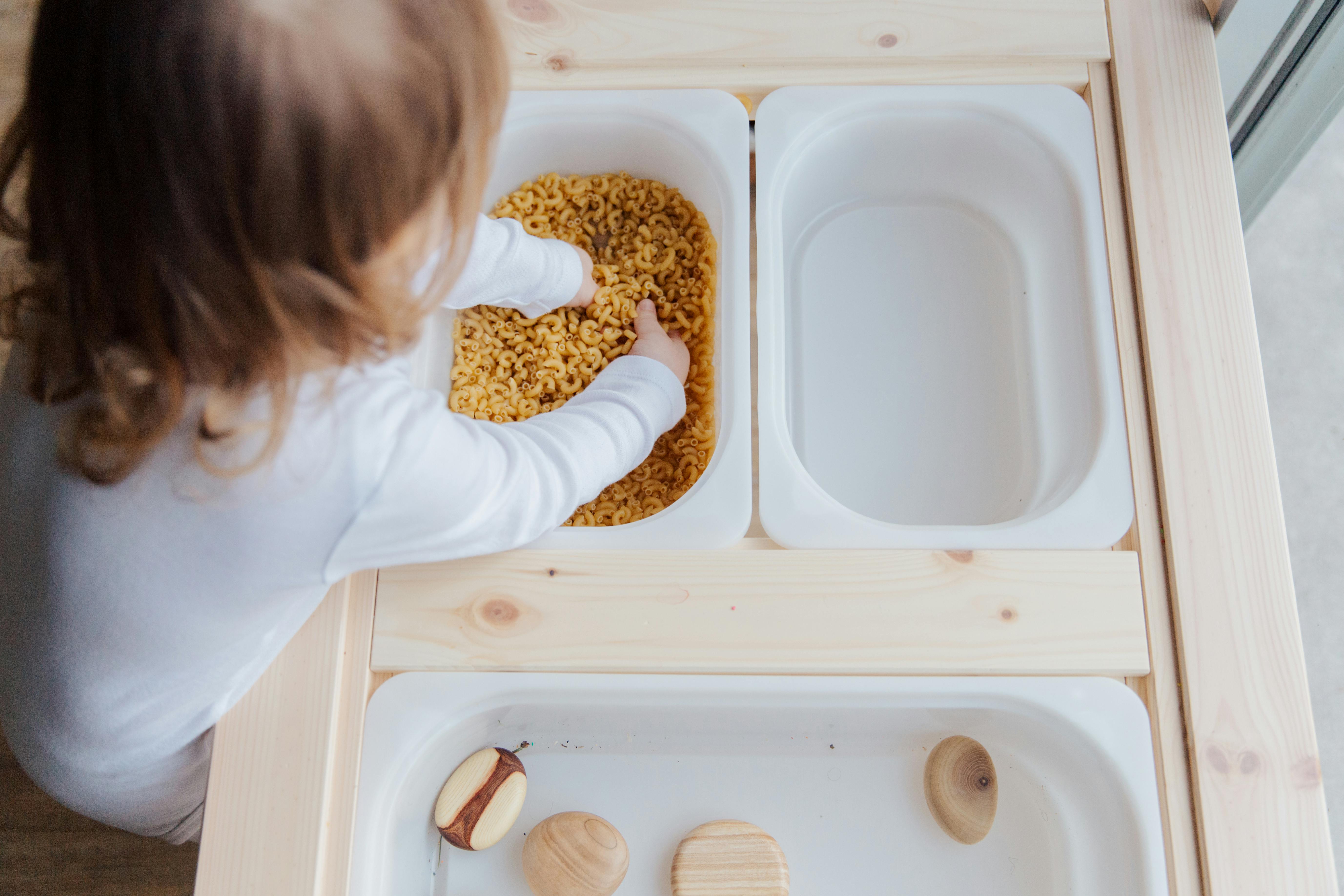 photo of child playing with macaroni pasta