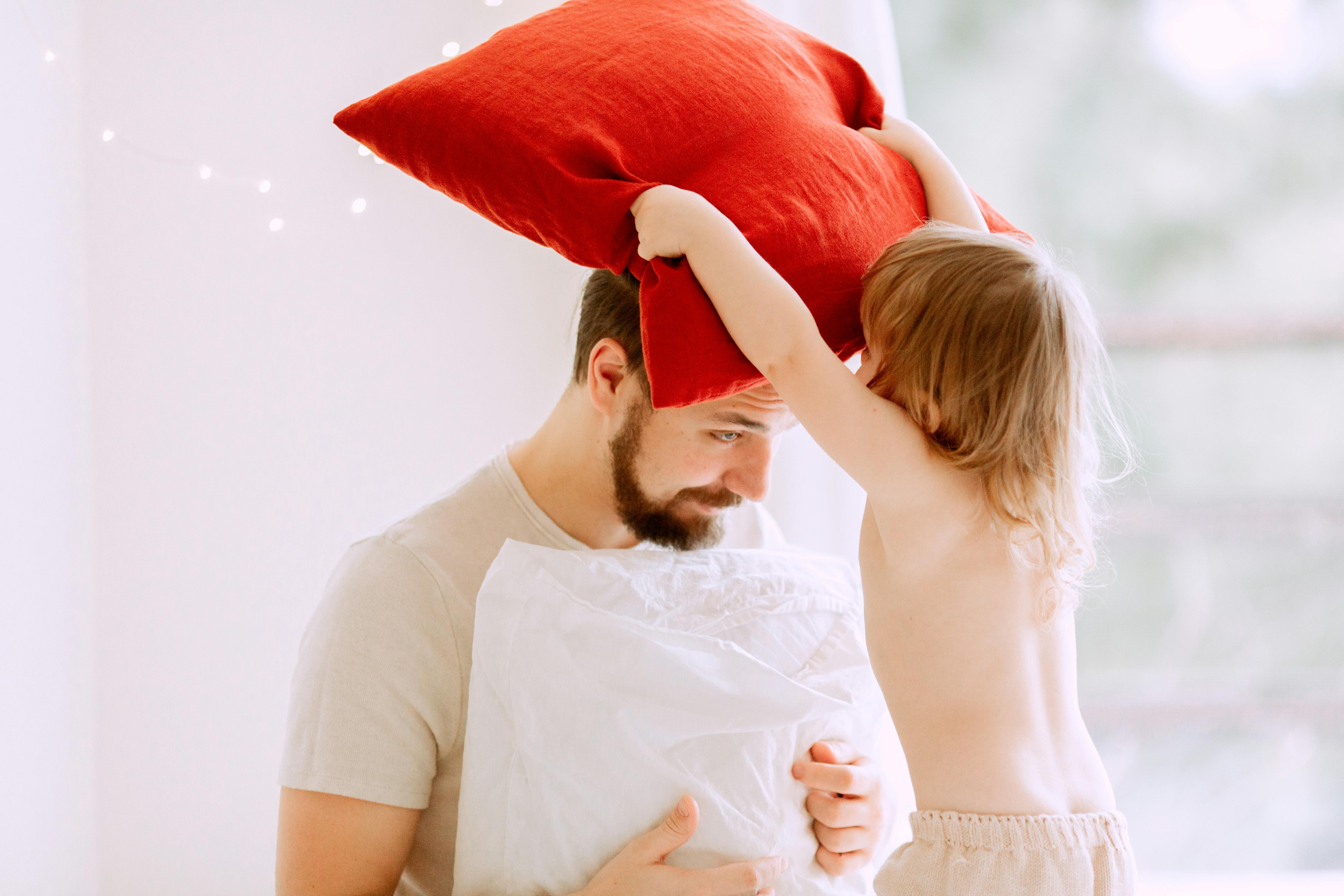 baby girl putting a red pillow on her father s head