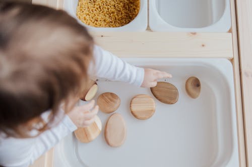 Free Crop anonymous child getting brown stones from white container at home Stock Photo