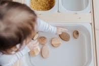 Crop anonymous child getting brown stones from white container at home