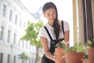 在阳光明媚的户外，一位微笑的女子正在照料盆栽植物