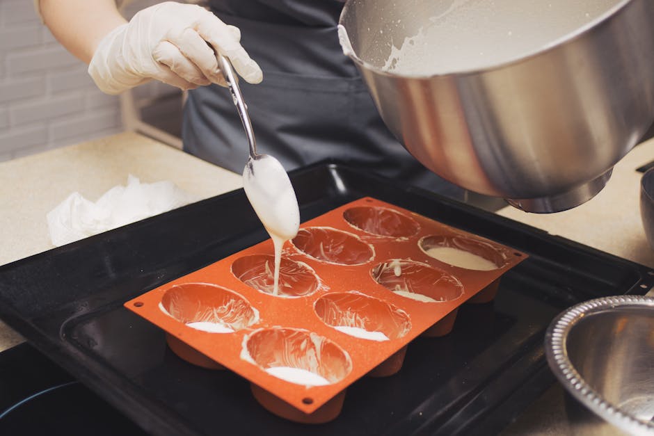 Vaihe vaiheelta: Valmistusohje ja valokuvausvinkit Vaihe vaiheelta: Valmistusohje ja valokuvausvinkit - Chef wearing gloves pours batter into silicone molds, preparing for baki