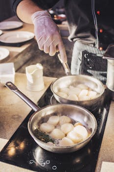 A chef uses a stove to sauté fresh scallops in a professional kitchen with precise technique.