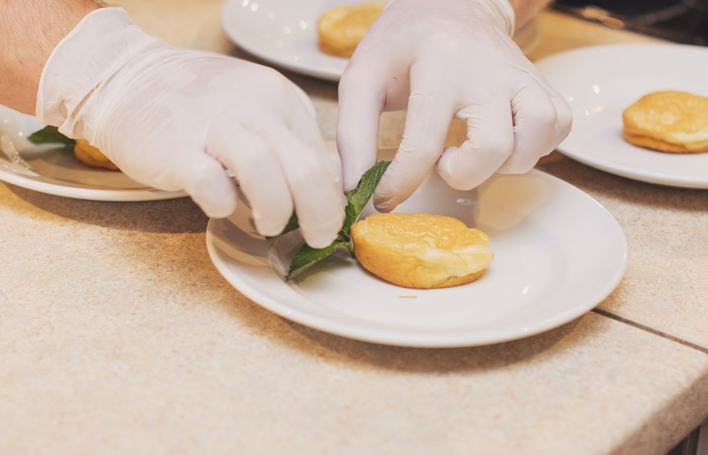 Close-up of a chef's hands decorating pastries with mint leaves in a restaurant kitchen.