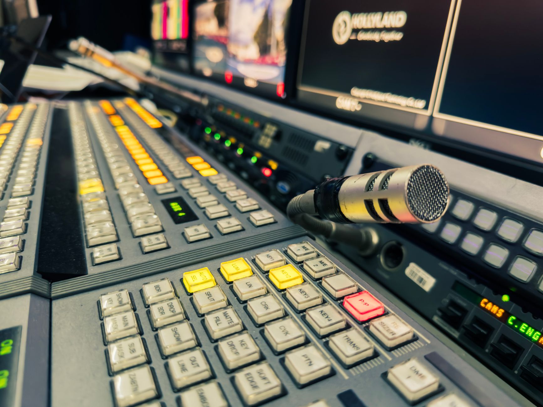 Detailed view of a broadcasting studio control panel with a microphone and multiple screens.