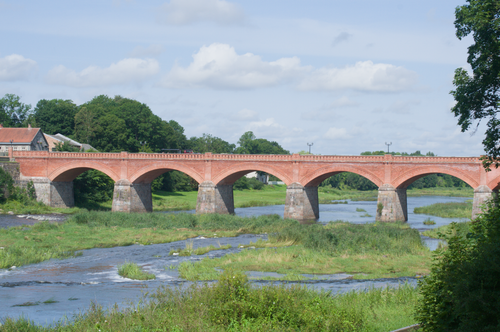 Free Charming red brick arch bridge over a lush green river in Ventspils, Latvia. Stock Photo