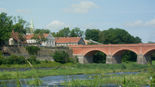 Free Scenic view of a historic red brick bridge and riverside village under clear sky. Stock Photo