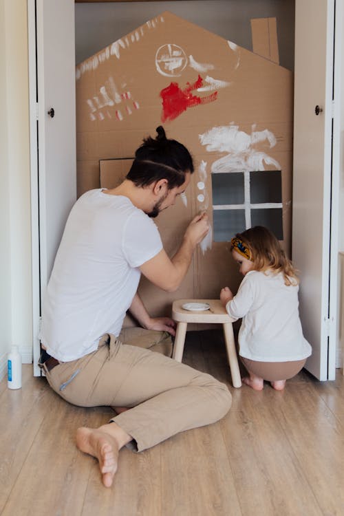 Free Father and Daughter Painting a Cardboard House Together  Stock Photo