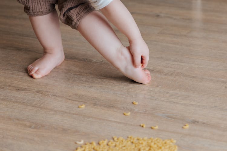 Anonymous Toddler Trying To Remove Stuck Pasta From Foot While Developing Fine Motor Skills At Home