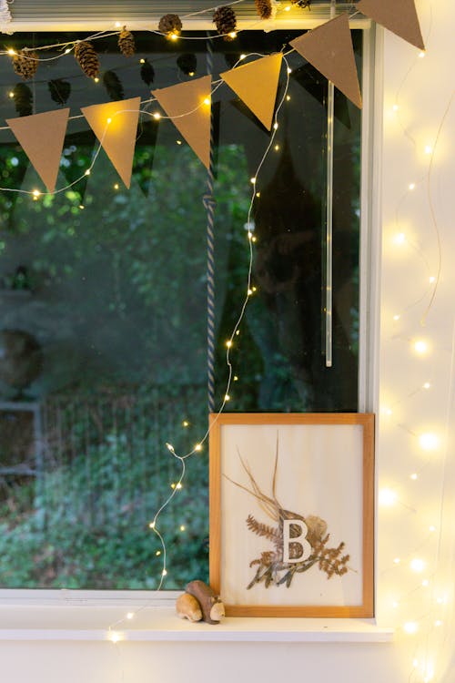 Window decorated with paper flags garlands and cones for celebrating Christmas and photo frame with B letter on windowsill