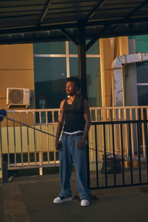Free Young man standing under a structure, casually posing in an urban setting at sunset. Stock Photo