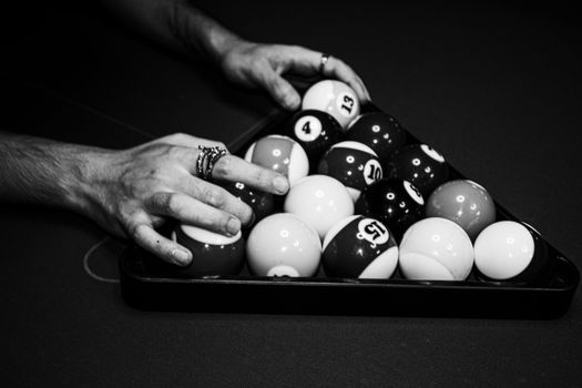 Close-up of hands setting up billiard balls on a pool table in black and white.