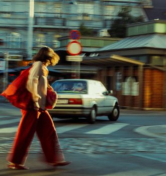 A woman in red clothing crosses a city street with motion blur effect.