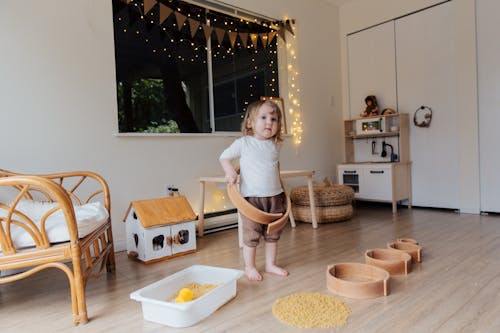 Toddler girl playing with wooden shapes of different size and pasta while trying to put biggest shape on