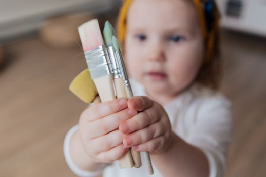 一个可爱的幼儿在室内拿着几支画笔，正享受创作的乐趣