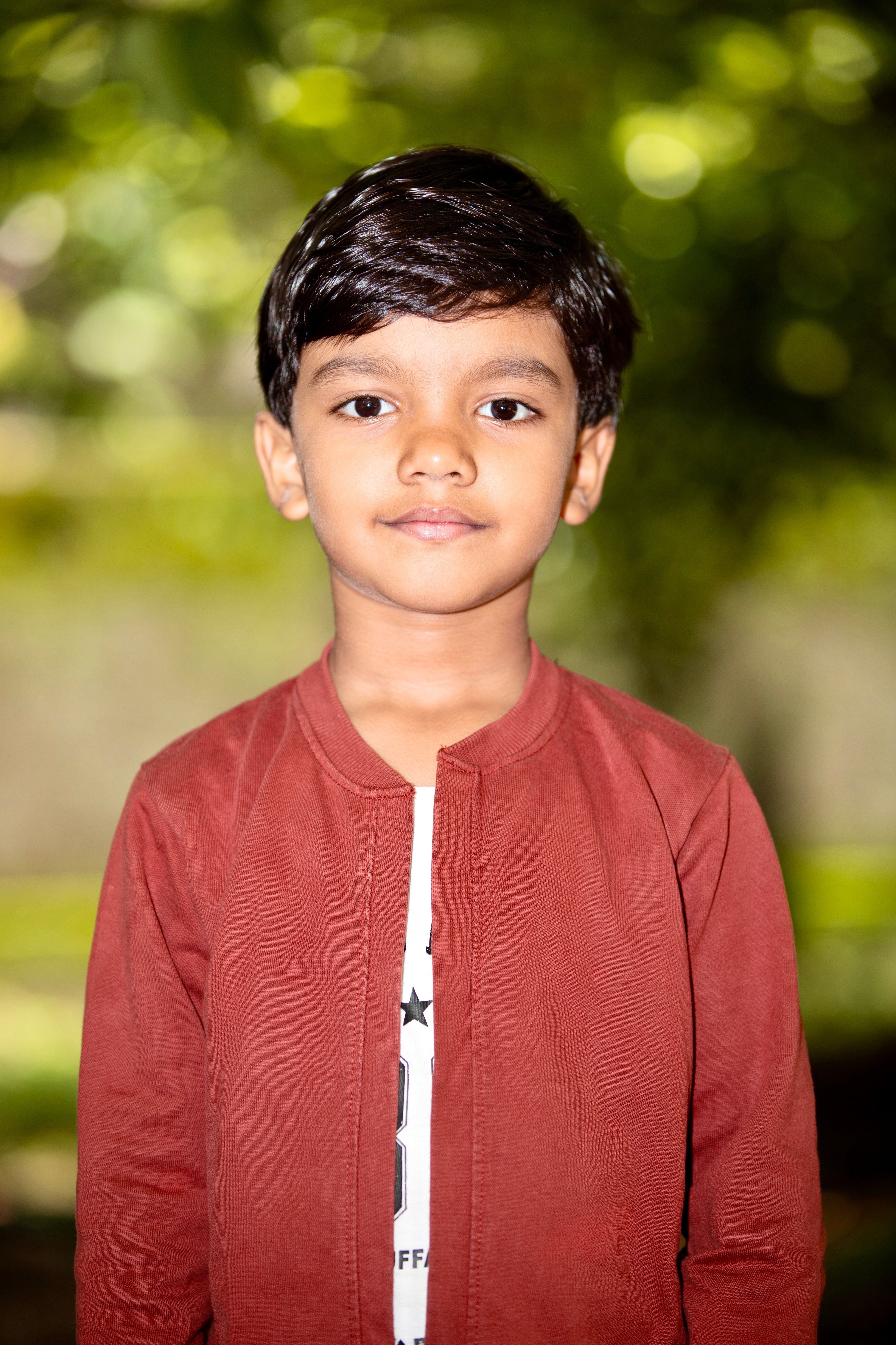 Charming portrait of a young boy standing outdoors against a blurred green backdrop.