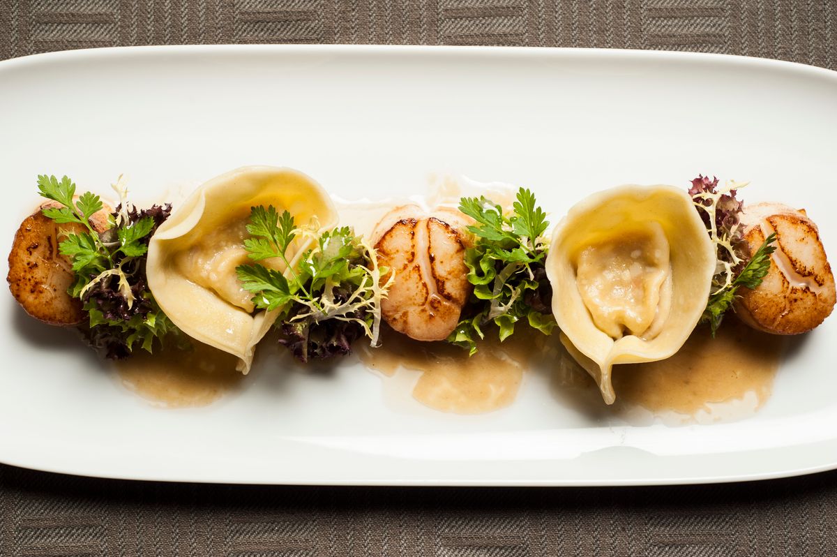 Long white plate with alternating seared scallops, large tortellini, microgreens and a light brown sauce