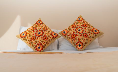 Two orange floral embroidered cushions on a bed