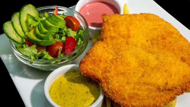 Golden schnitzel served with a vibrant salad and dipping sauces.