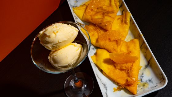 Folded crepes glazed with orange sauce and segments beside a glass of vanilla ice cream scoops