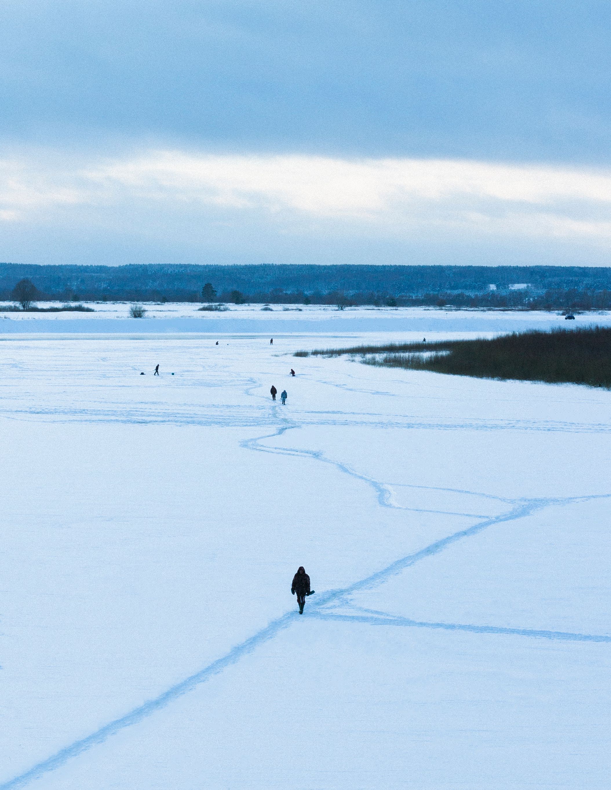 People walking on a vast snow-covered field under a cloudy winter sky.