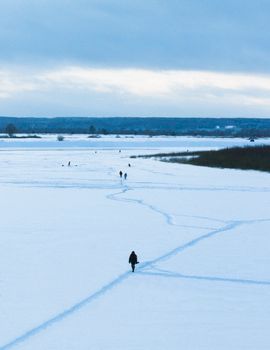 People walking on a vast snow-covered field under a cloudy winter sky.