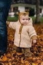 迷人的婴儿穿着舒适的夹克在户外探索秋天的叶子，展现出纯真与嬉戏