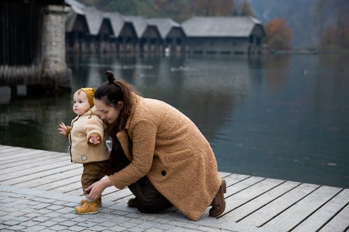 Woman in Brown Coat Kneeling on Brown Wooden Dock