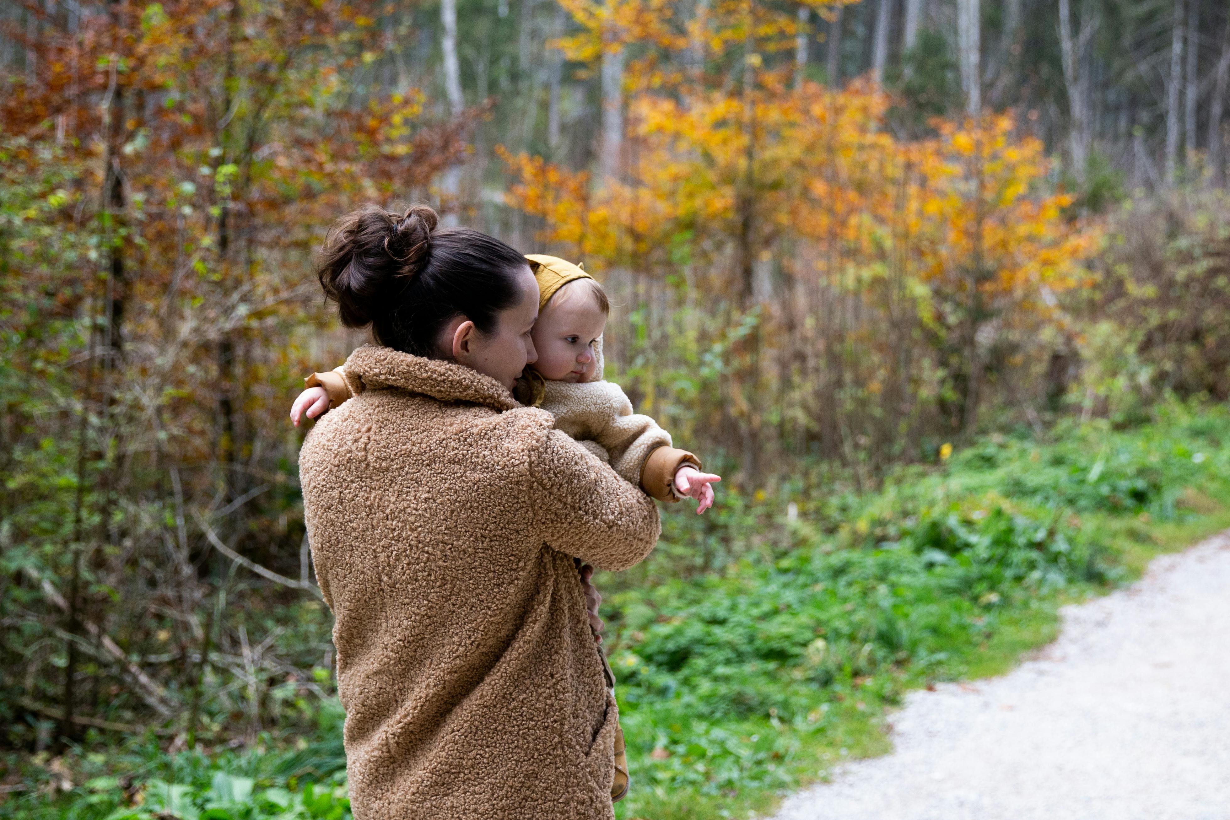 woman in brown sweater carrying baby in brown sweater