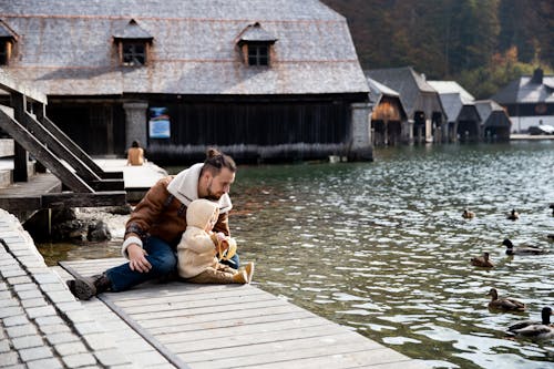 Free Photo Of Man And Baby Sitting On Wooden Dock  Stock Photo