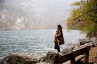 一位母亲抱着孩子，凝视着宁静的秋日湖面，四周被大自然环绕