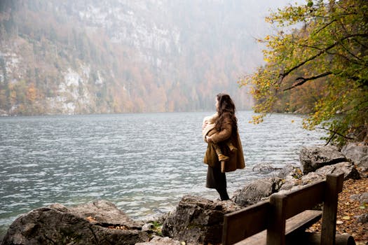 一位母亲抱着孩子，凝视着宁静的秋日湖面，四周被大自然环绕