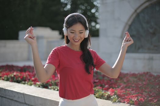 一个快乐的女人在阳光明媚的花园里戴着耳机跳舞，感觉轻松愉快