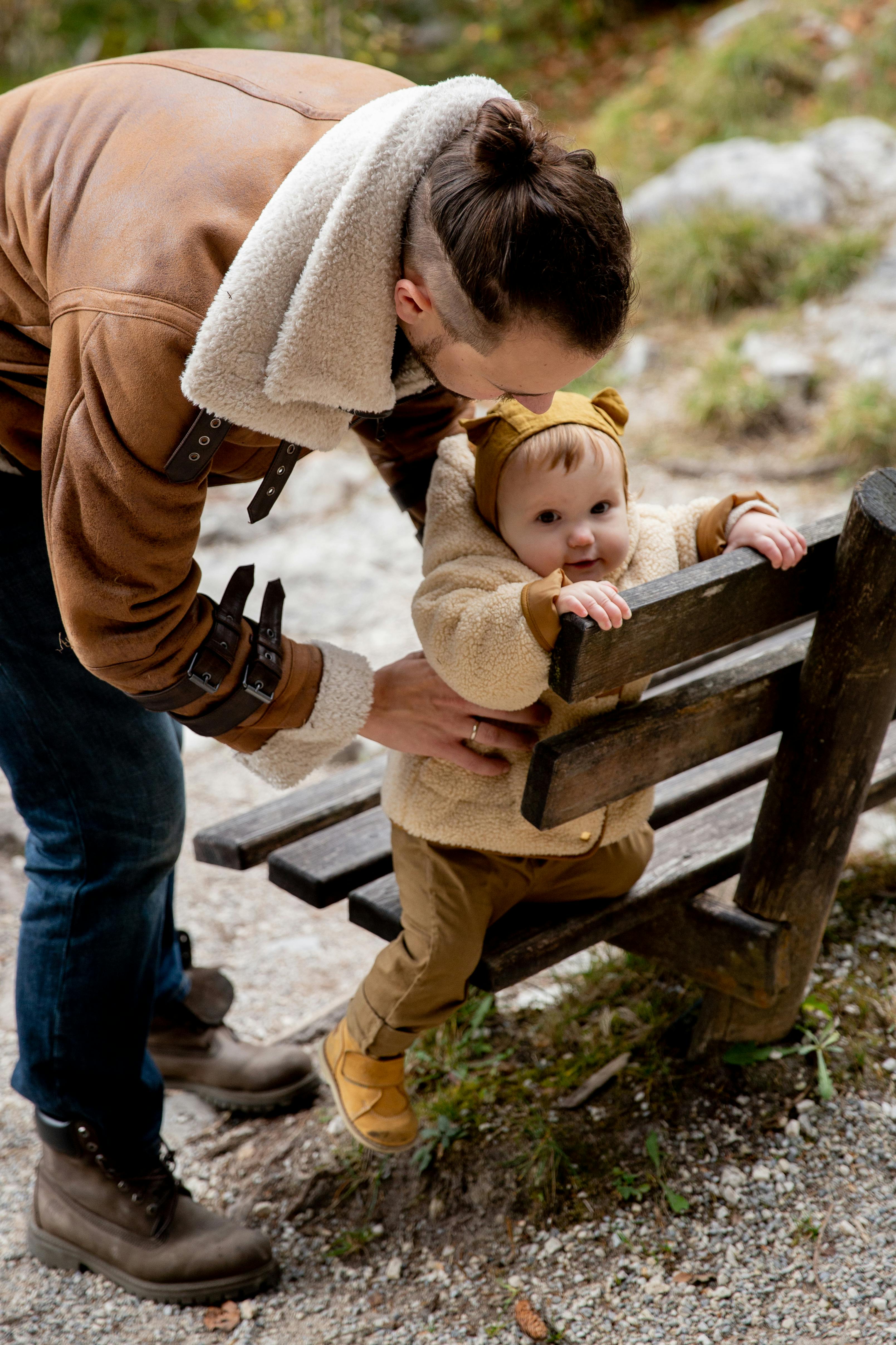 photo of baby holding on wooden bench