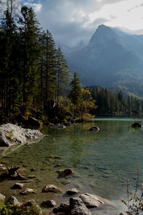 Free Tranquil alpine lake scene with pine trees and majestic mountains in the background. Stock Photo