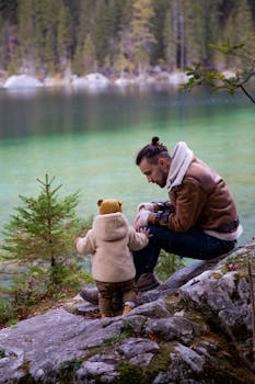 父亲和蹒跚学步的孩子在风景如画的湖边，于郁郁葱葱的绿树间享受宁静的时刻