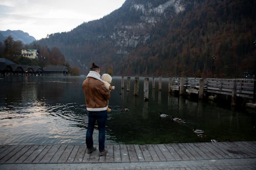 Free Photo Of Man Carrying Baby Standing On Wooden Dock  Stock Photo