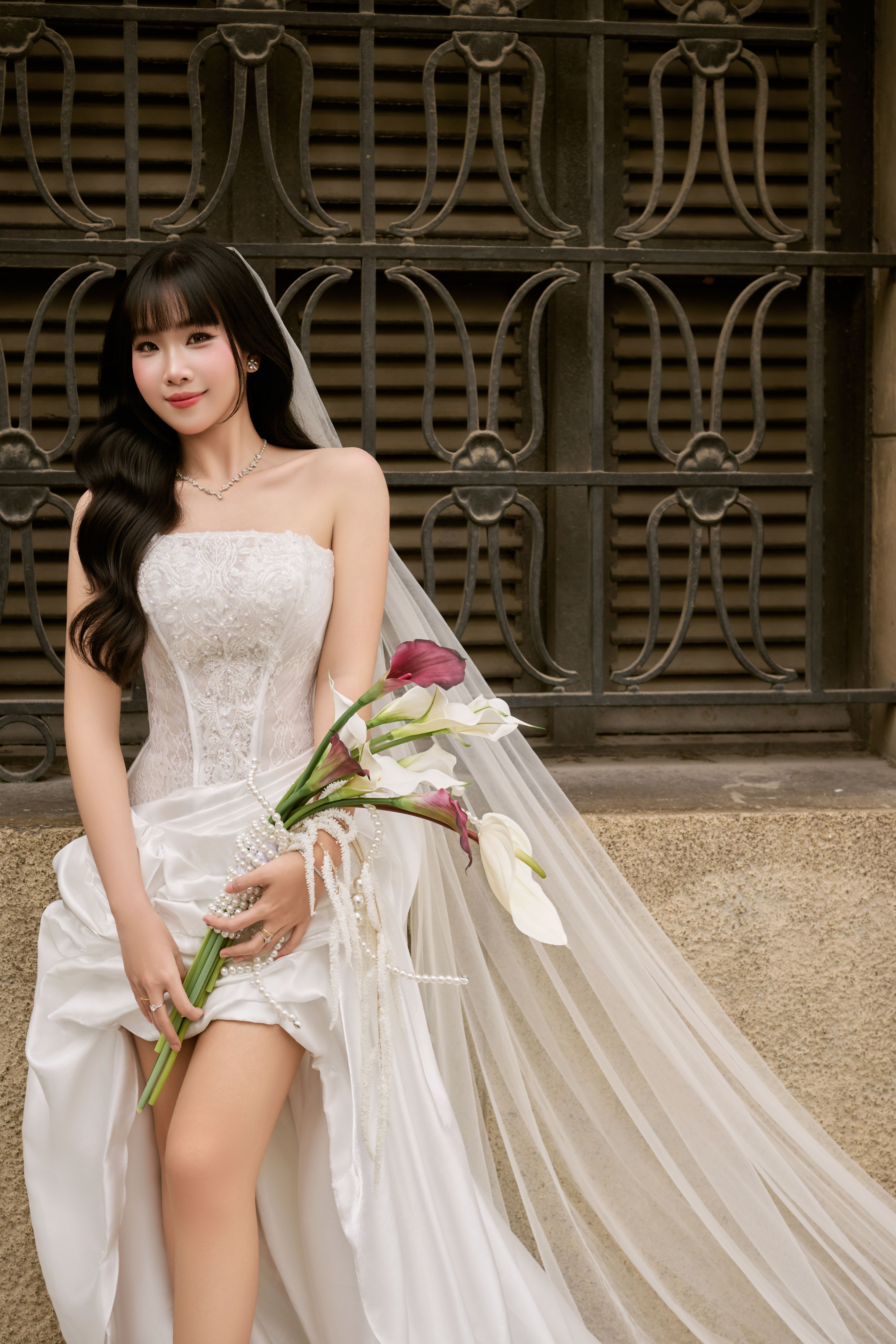 A beautiful bride in a white wedding dress holding flowers, posing elegantly against an ornate iron fence.