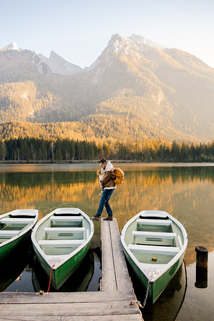 Father With Kid On Hands Standing On Wooden Pier Near Boat On Lake Shore