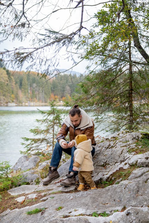 Father with little kid resting on rocky cliff near lake in forest