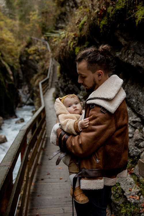 Father and little baby standing on wooden pathway above mountain river