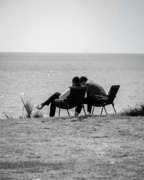 Free Black and white photo of two people sitting together by the seaside enjoying a peaceful moment. Stock Photo