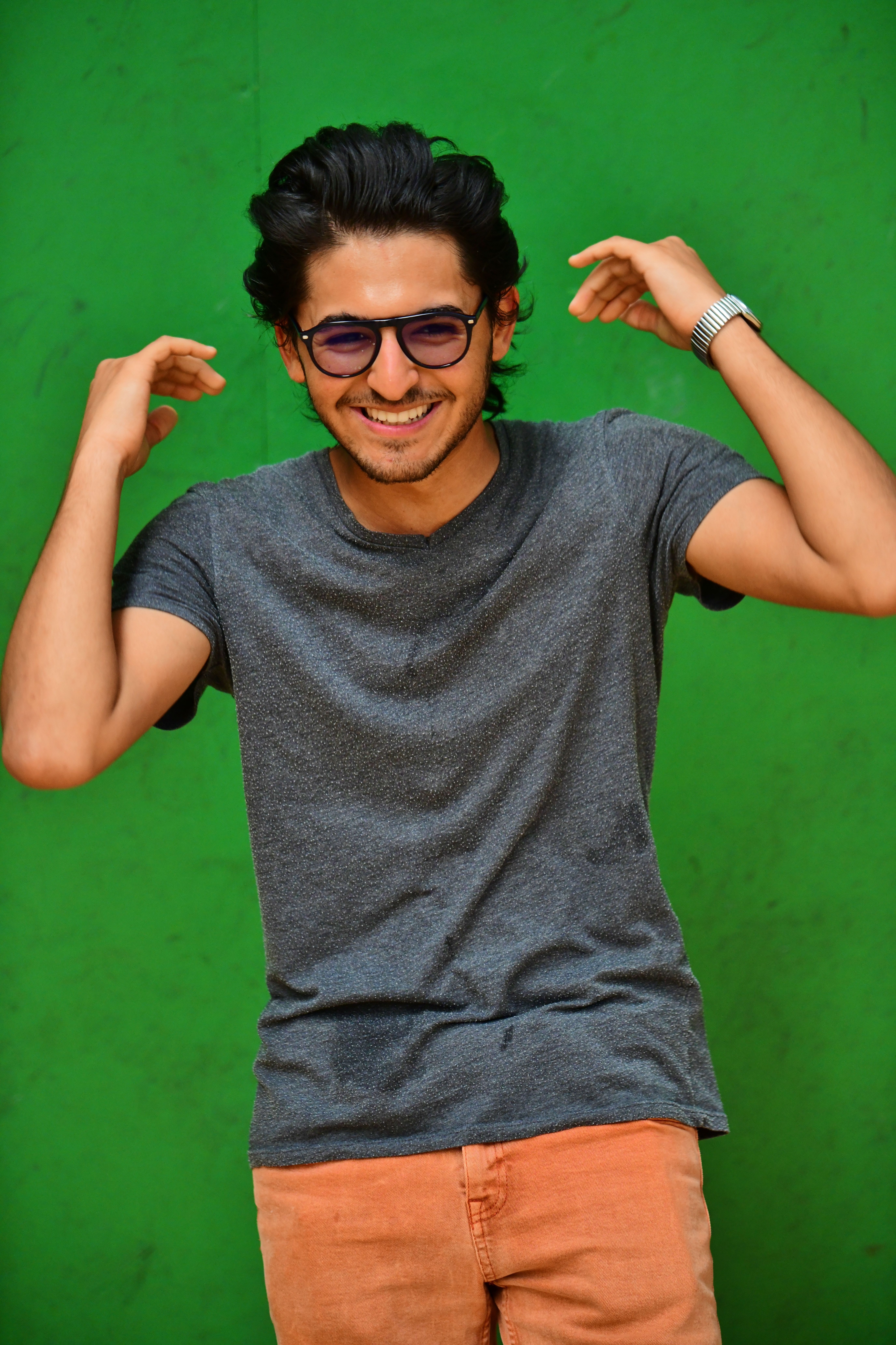 A cheerful young adult male poses confidently against a vibrant green wall.
