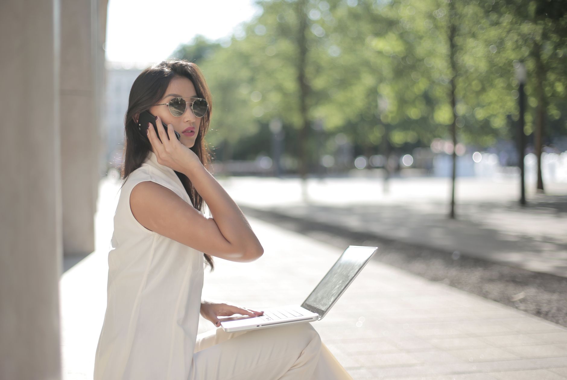 Confident woman sitting outdoors with laptop and phone, working remotely.