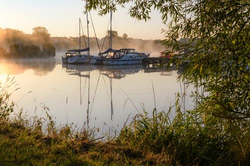 Free Misty morning scene at a riverside dock with boats gently floating, creating a peaceful ambiance. Stock Photo
