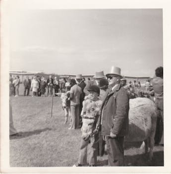 一张复古照片中，一群戴着高顶帽子的人在户外，展示了一场老式活动