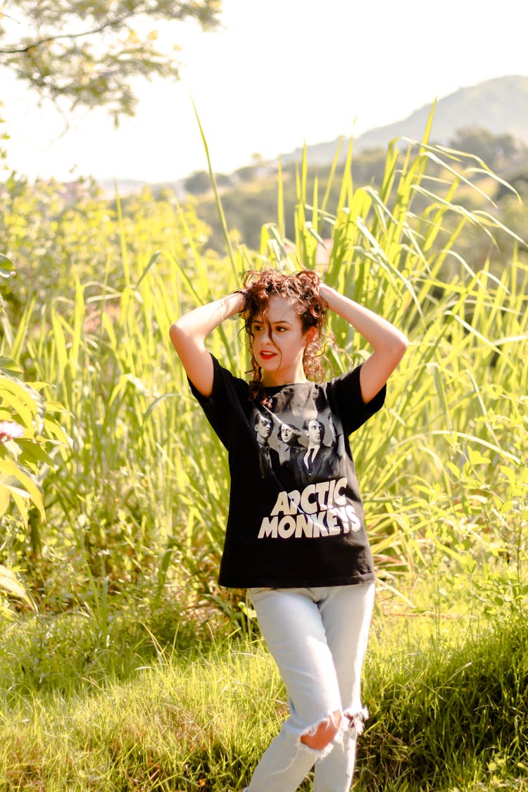 Woman In Black And White T-shirt And Tattered Pants Standing On Green Grass Field